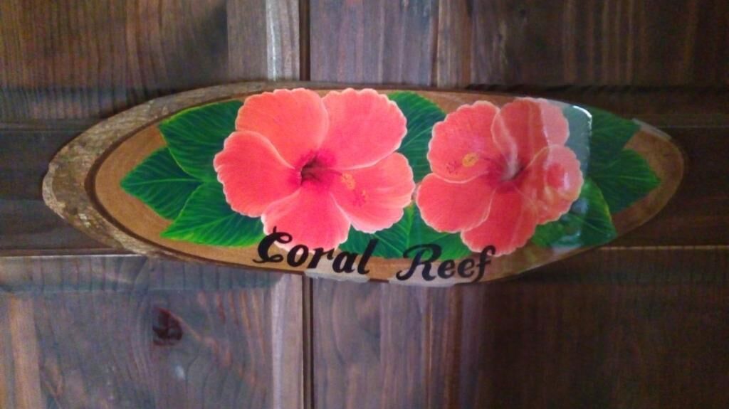 Una placa de madera con dos flores rosadas y el texto 'Coral Reef'.