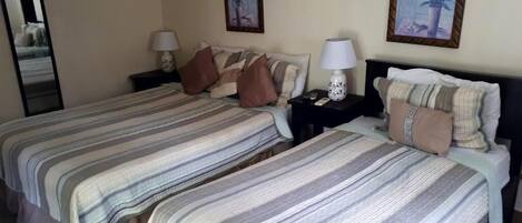 A hotel room with two beds, each with striped bedding and pillows, a nightstand with a lamp, and framed artwork on the walls.