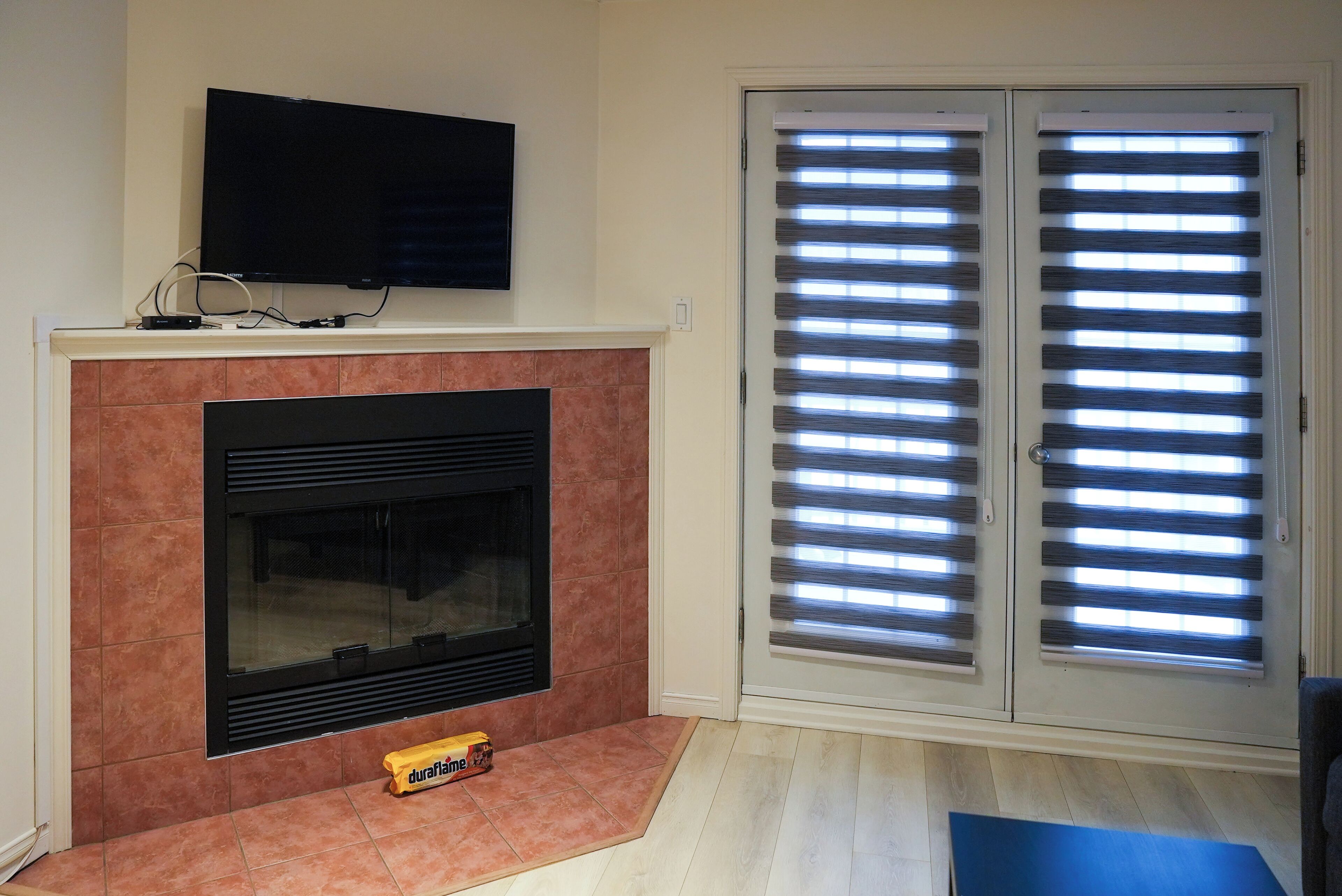 A living room with a fireplace, a flat-screen TV mounted above it, and a sliding glass door with blinds.