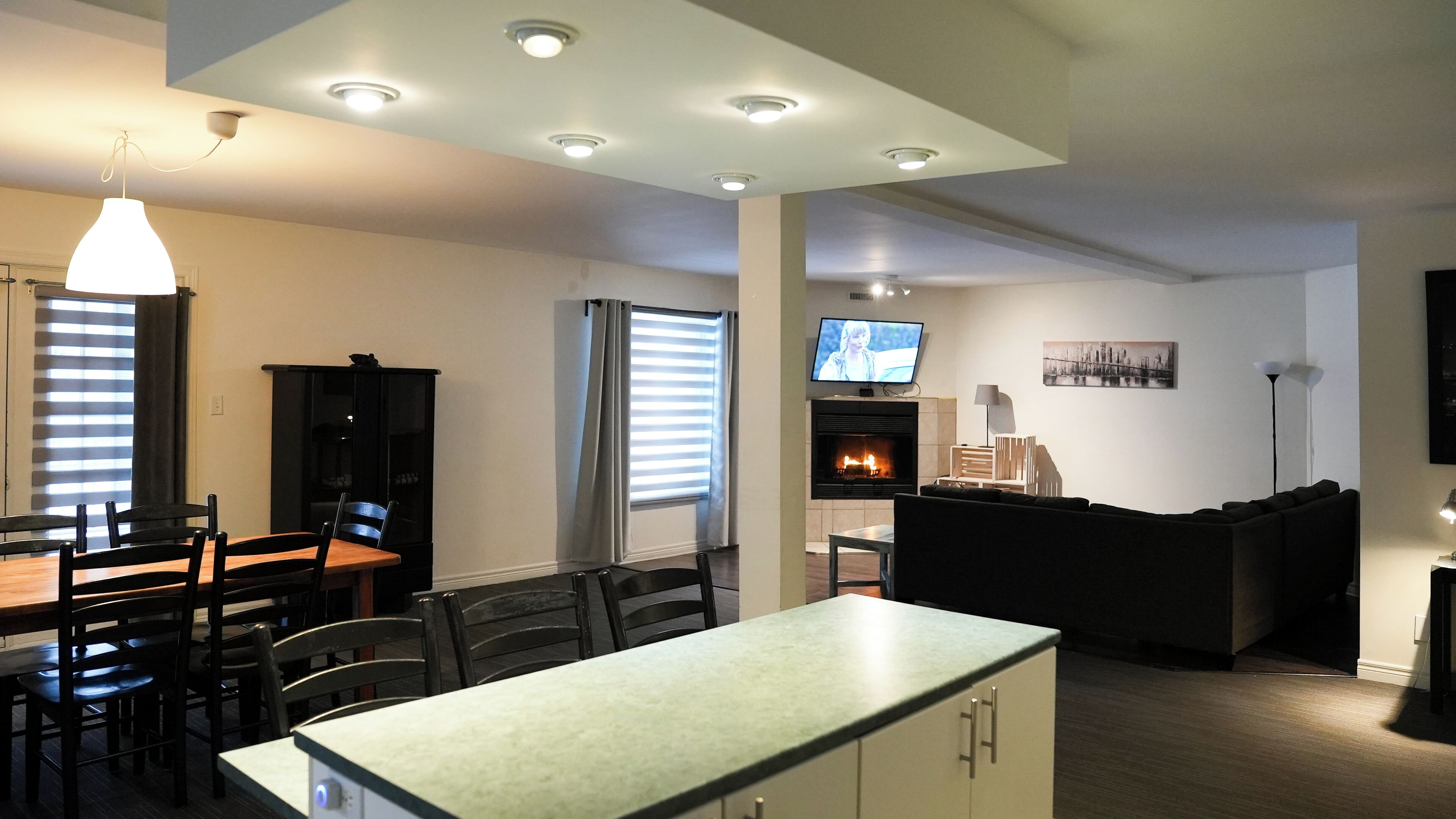 A modern living room with a fireplace, a dining area with a table and chairs, and a TV mounted on the wall.