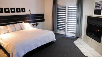 A hotel room with a large bed, a fireplace, a sliding glass door with curtains, and framed pictures on the wall.