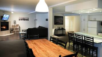 A modern living room with a fireplace, a dining area with a wooden table and chairs, and a kitchen with white cabinets.