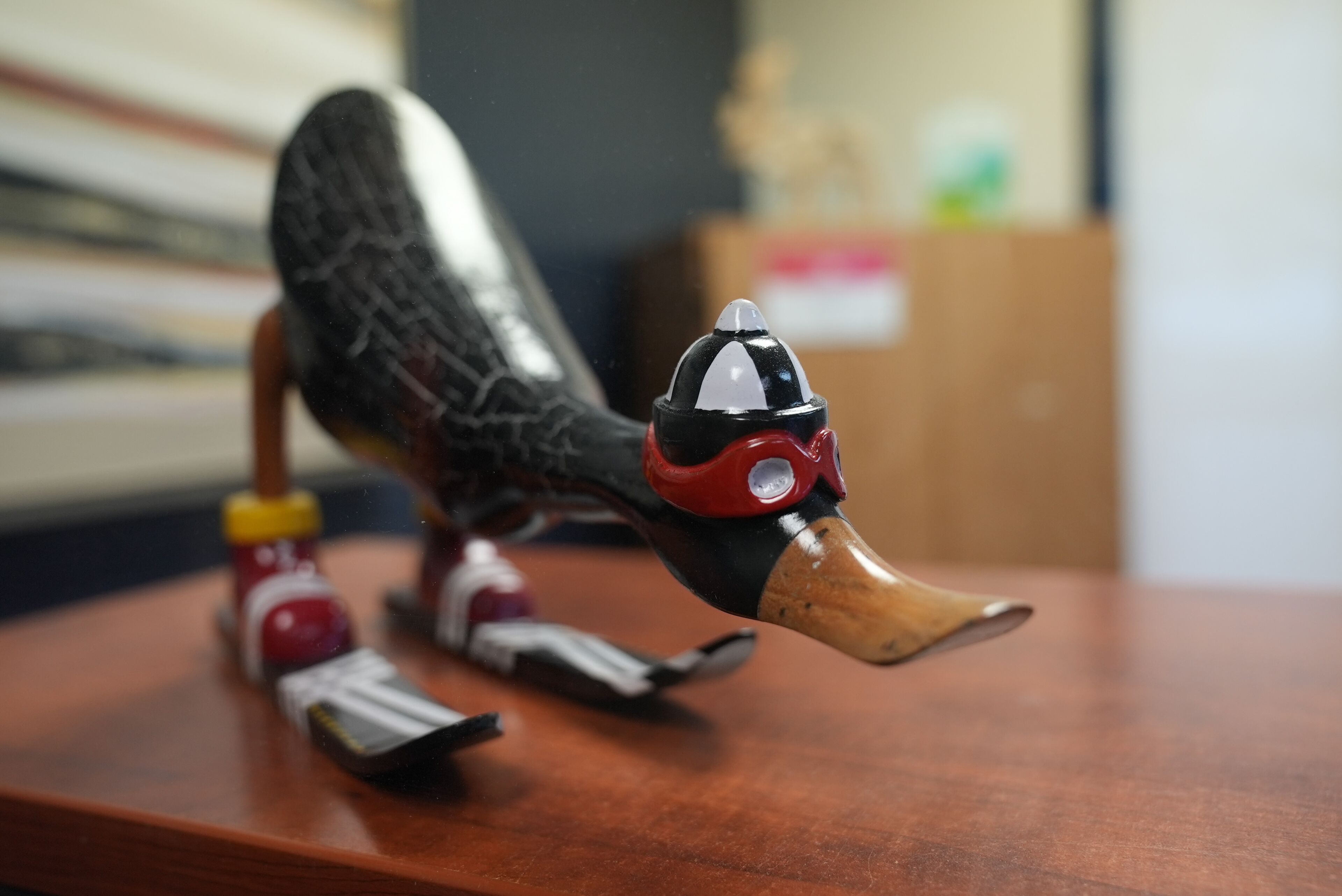 Una escultura de madera de un ave con la cabeza roja y negra, un pico de madera y el cuerpo rojo y blanco.