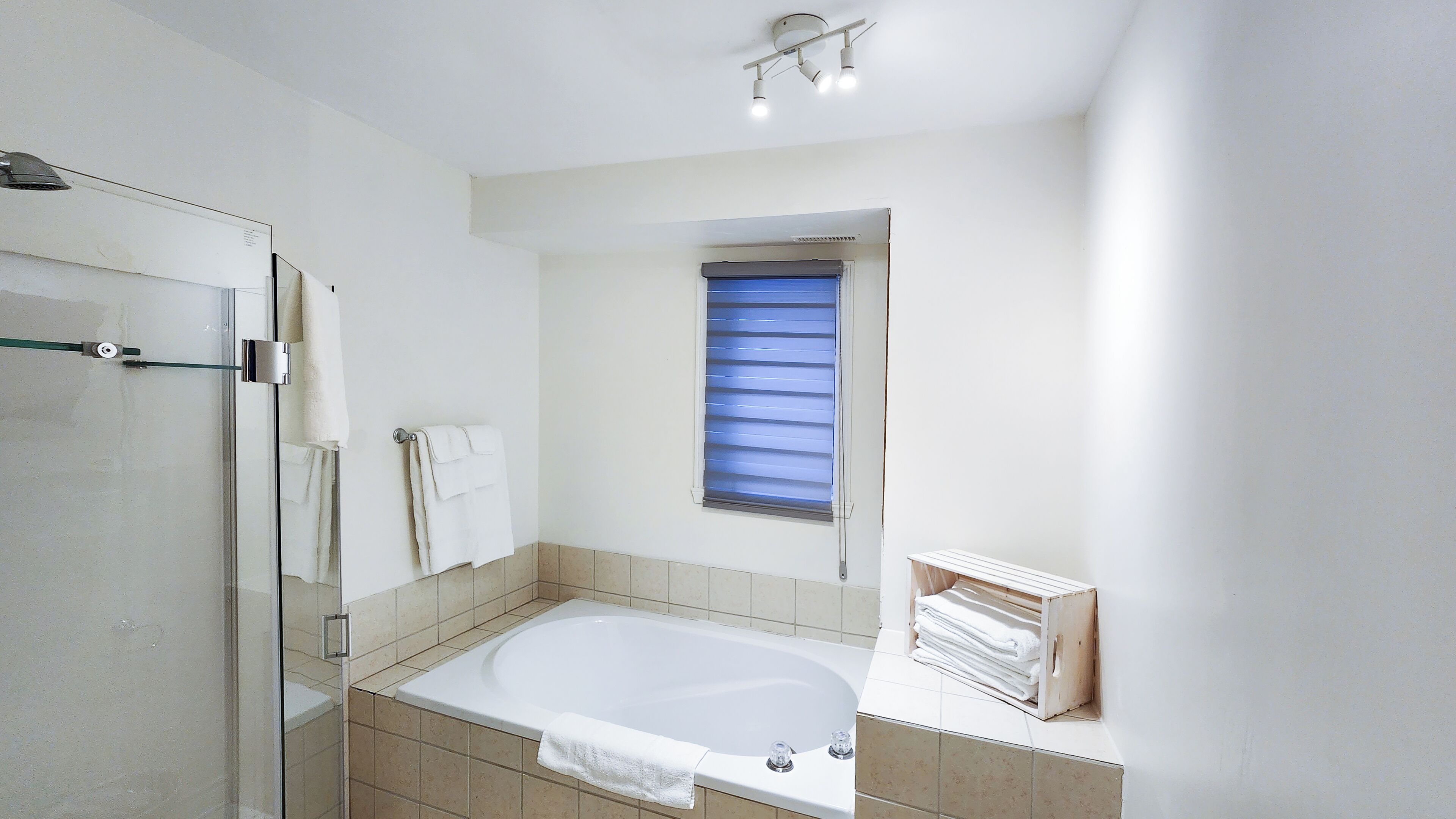 A modern bathroom with a glass shower enclosure, a bathtub, and a window with blinds.