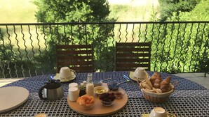 A table set with breakfast items, including bread, fruit, and coffee cups, on a balcony with a view of greenery. - Gite Stéphanie l'Ephedra – Charming 3-Star Home with Pool in Sampzon (Sampzon)