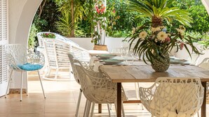 Un espacio de comedor al aire libre con sillas de mimbre blanco y una mesa de madera listo para dos personas.