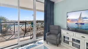 A balcony with a view of the sea, a TV on a cabinet, and a grey armchair. - Azure #112 (Fort Walton Beach)