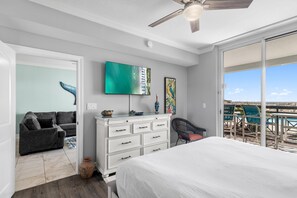 A bedroom with a bed, a dresser, a TV, and a balcony with chairs.