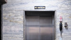 An elevator with a "NO SMOKING" sign above it, a phone, and a potted plant beside it.