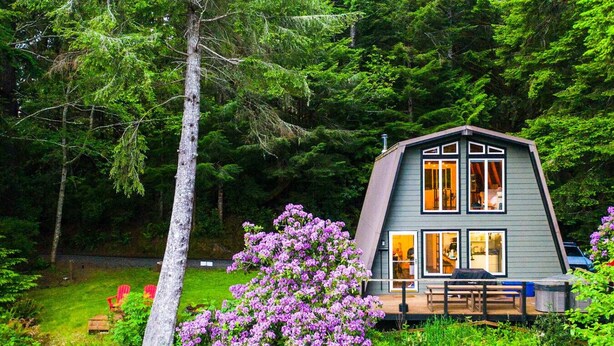 A modern, two-story cabin with a sloped roof, surrounded by lush greenery and a flowering bush. - 2 Homes-14 Acres+2 Spas +Lake Access+Kayaks (Lakeside)