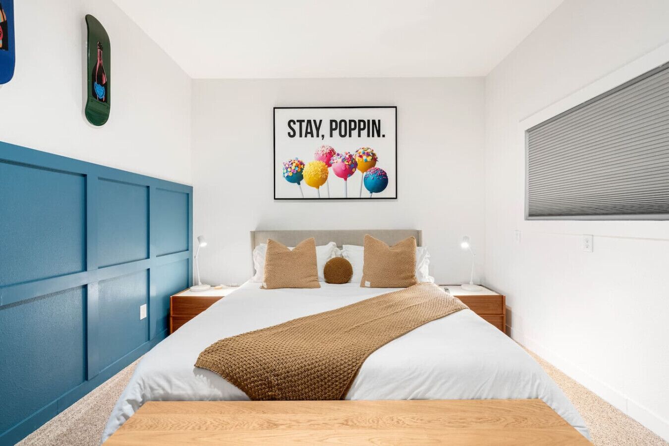 A bedroom with a bed, a blue wardrobe, a wall art piece, and a window with blinds.