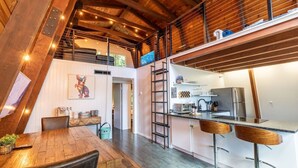 A modern kitchen with a central island, a dining area with a wooden table and chairs, and a loft bedroom with a sloped ceiling. - 2 Homes-14 Acres+2 Spas +Lake Access+Kayaks (Lakeside)
