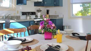 Eine moderne Küche mit türkisfarbenen Schränken, einem weißen Herd und einem Esstisch, gedeckt für ein Frühstück mit Früchten und einer Blumenvase.