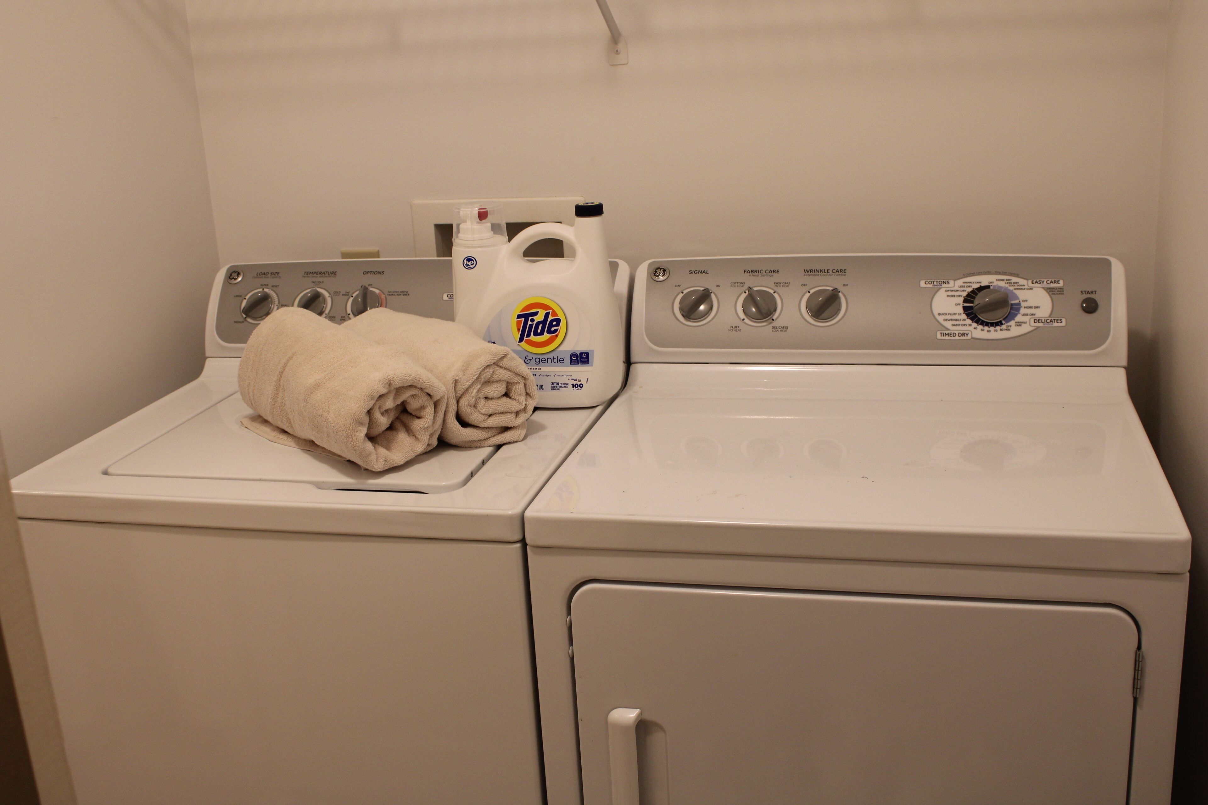 Une machine à laver à chargement frontal, avec du détergent Tide et une serviette pliée posée sur le dessus.