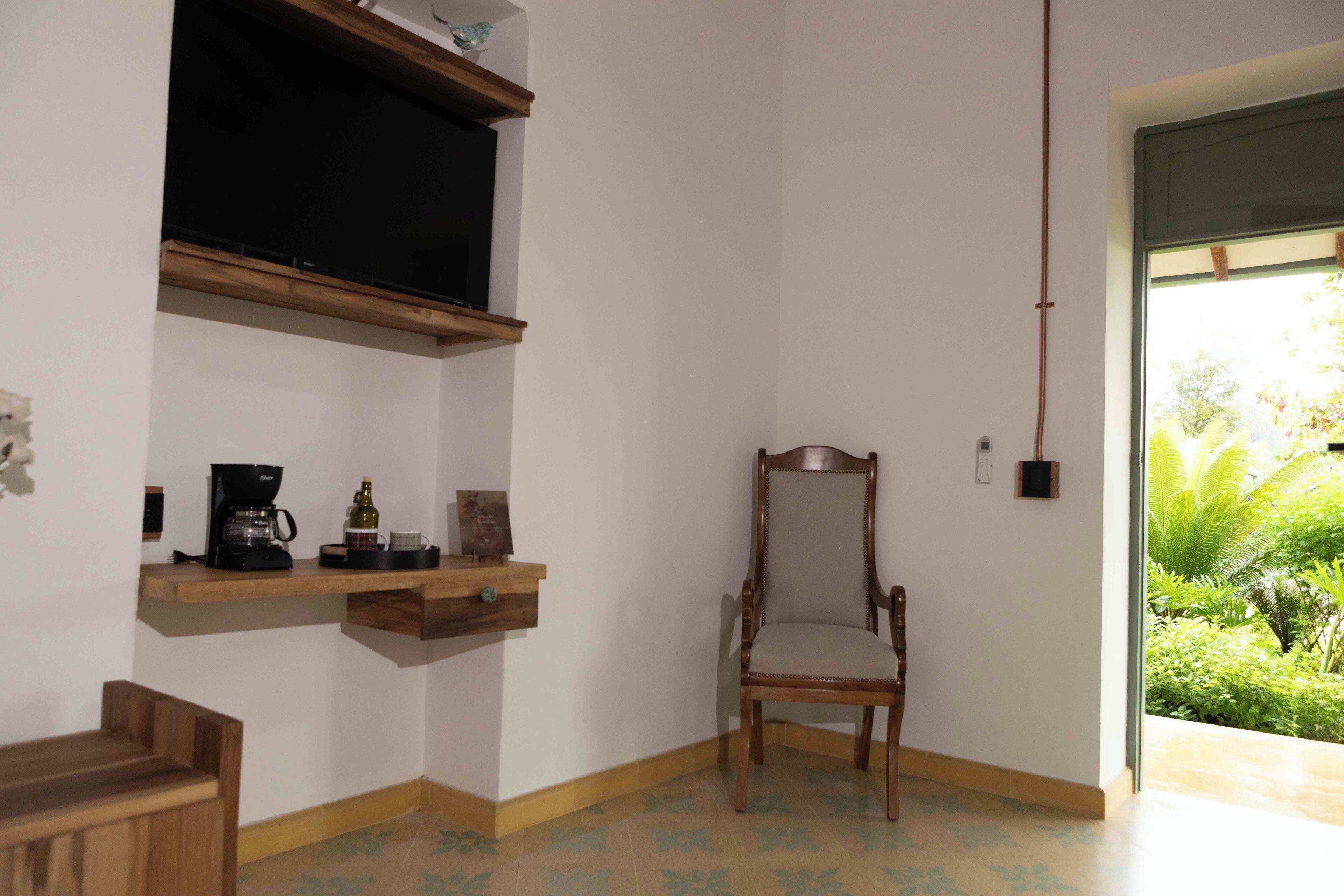 A room with a wooden chair, a coffee maker, and a shelf with a television.