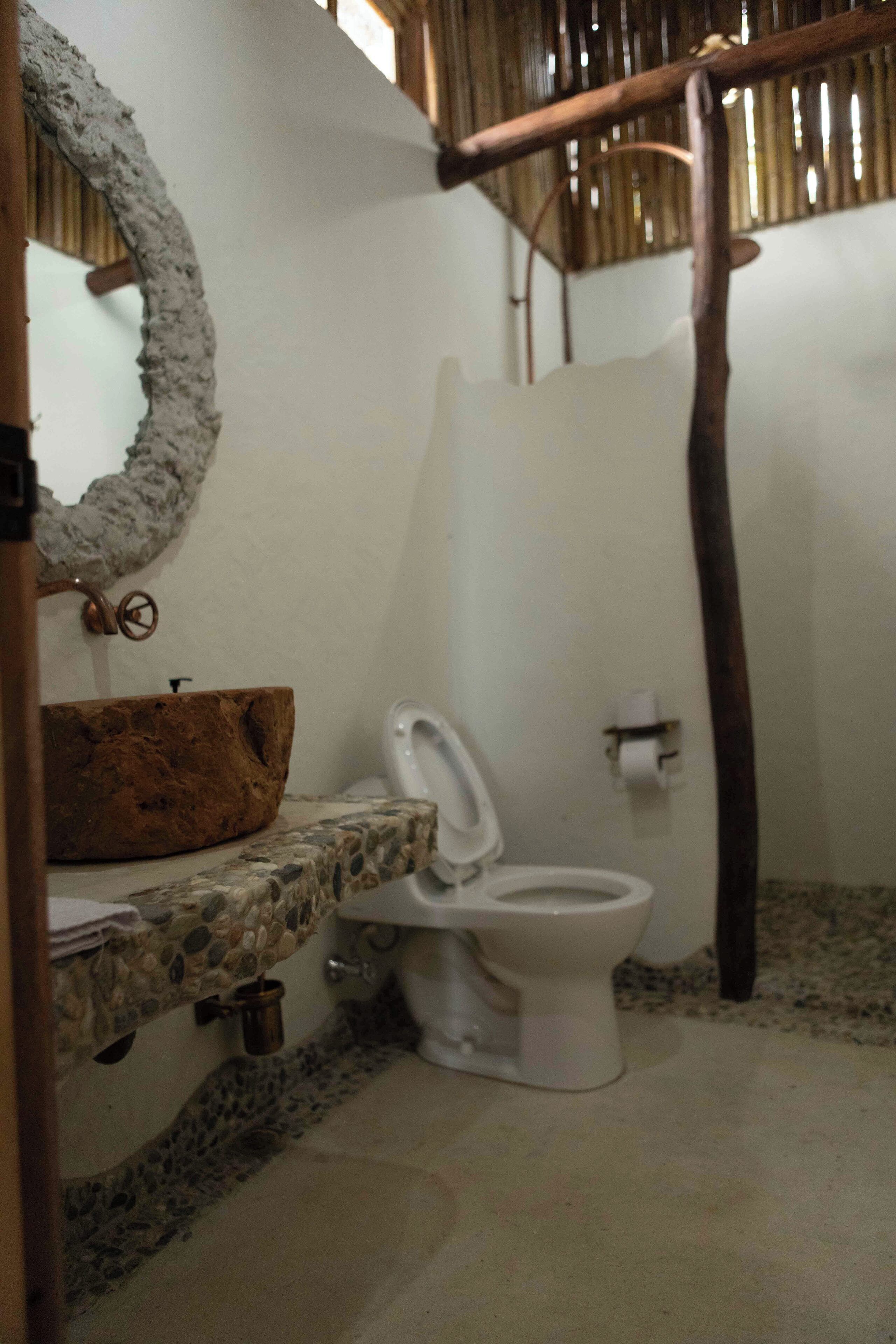 Een badkamer met een rustieke inrichting, met een stenen wasbak, een wit toilet en een houten douchecabine.