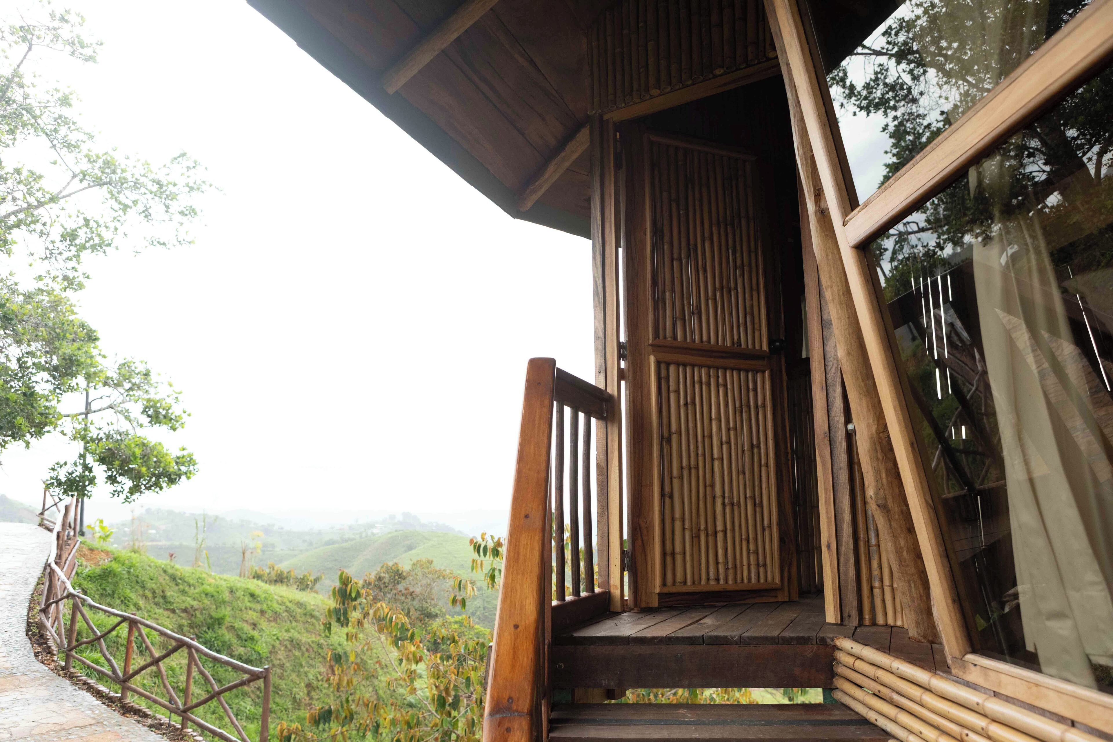 A wooden staircase leading to a covered entrance with a view of a lush green landscape.