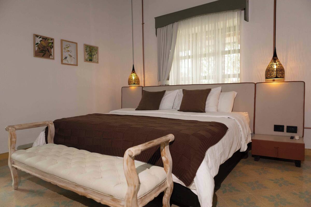 A bedroom with a large bed, two bedside tables, a wooden chair, and wall art.