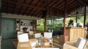 A covered outdoor seating area with wooden furniture and a view of greenery.