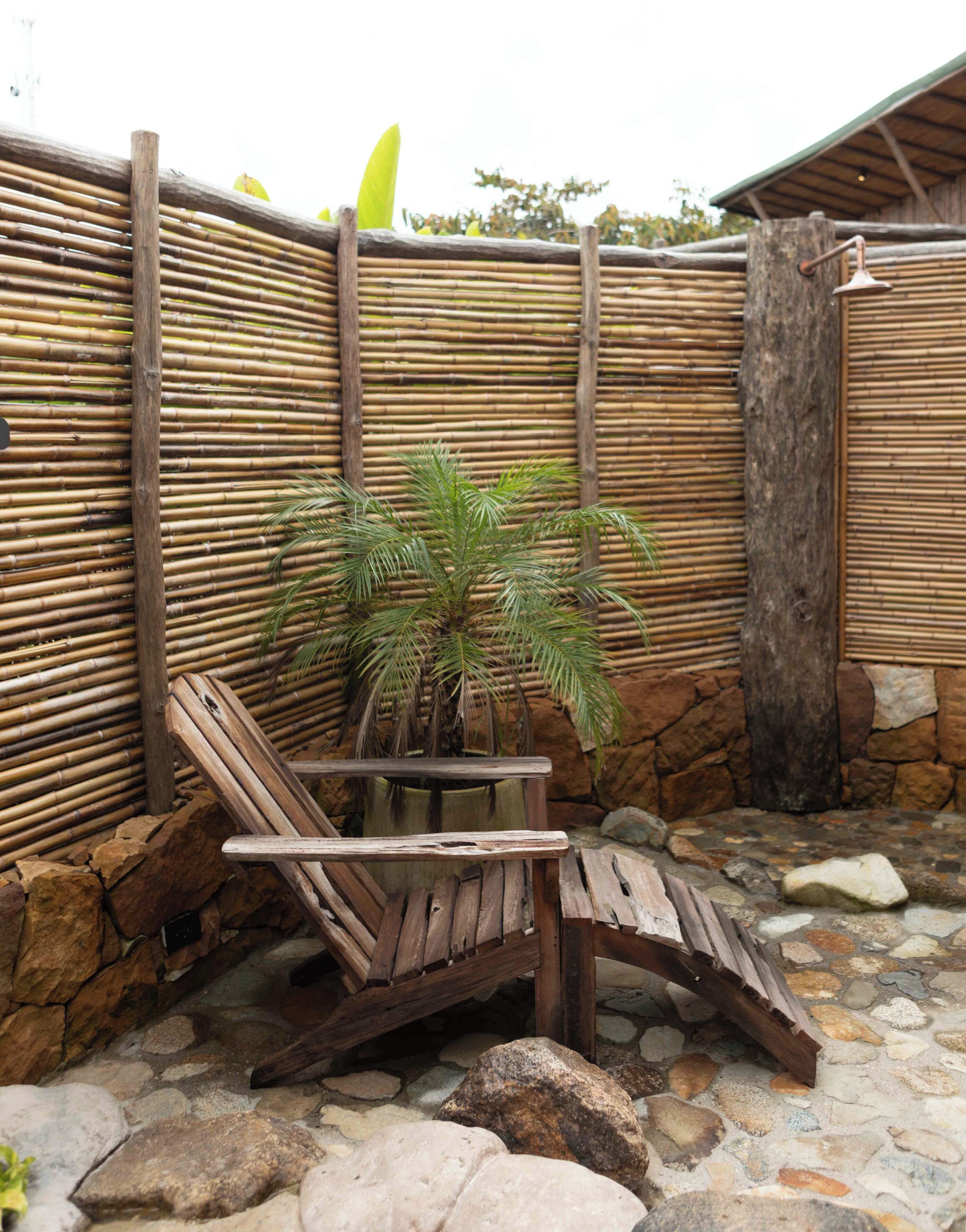 A wooden bench and a small table with a plant in a stone and bamboo outdoor area.