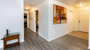 Un couloir avec un plancher en bois, un tableau accroché au mur et une porte au fond.