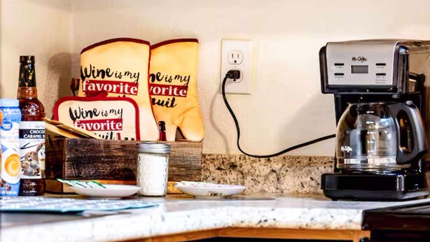 Un comptoir de cuisine avec une machine à café, une bouteille de vin et deux tabliers accrochés au mur.