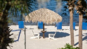 A beach with a thatched umbrella, white lounge chairs, and palm trees. - Gorgeous corner condo w premium lake/pool view! (Davenport)