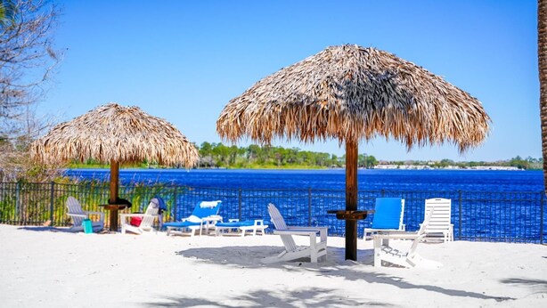 A beach with thatched umbrellas and lounge chairs facing a clear blue sea. - Gorgeous corner condo w premium lake/pool view! (Davenport)