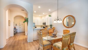 A dining area with wicker chairs and a glass table, a kitchen with white cabinets, and a round mirror on the wall. - Gorgeous corner condo w premium lake/pool view! (Davenport)