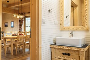 Un interior de madera con comedor, un lavamanos blanco y encimera negra, y un espejo con marco decorativo.