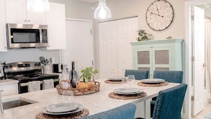 A modern kitchen with white cabinets, a central island with blue upholstered chairs, and pendant lighting.