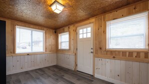 A room with wooden walls, large windows with blinds, a wooden door, and a light fixture on the ceiling. - Convenient location for adventures in the Adirondacks! (Warrensburg)