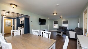 A spacious living area with a dining table, white chairs, a gray sofa, and a television mounted on the wall. - Convenient location for adventures in the Adirondacks! (Warrensburg)