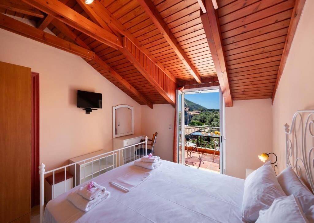 Un dormitorio con techo de madera, cama con ropa de cama blanca, televisor montado en la pared y balcón con vistas al paisaje.