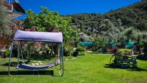 Un hamac dans un jardin verdoyant, agrémenté de plantes en pot, avec en arrière-plan une vue sur des maisons.
