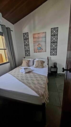 A bedroom with a bed, pillows, a blanket, a painting, and decorative panels.