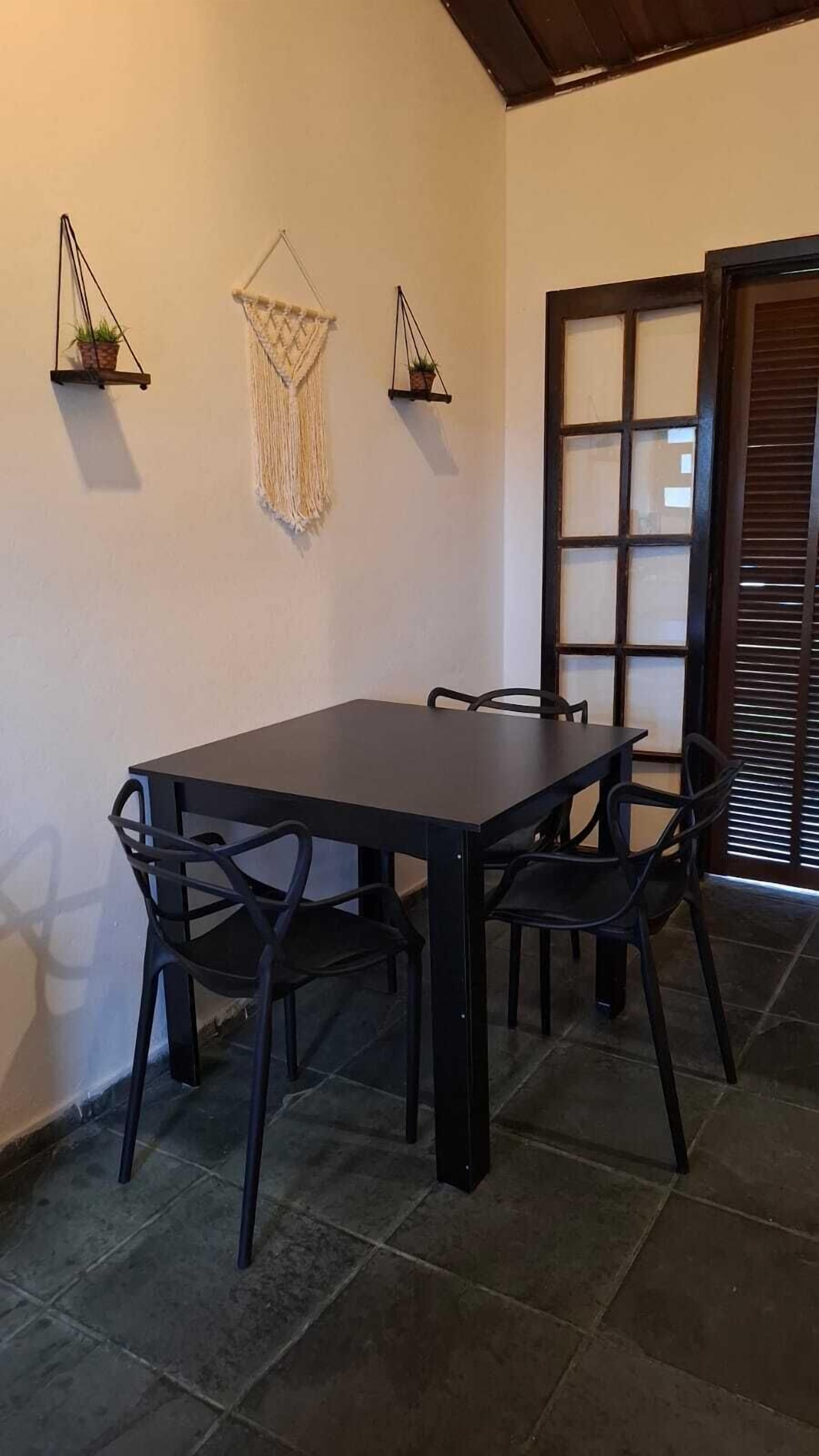 Uma área de refeições com uma mesa de madeira escura, quatro cadeiras e três plantas fixadas na parede.