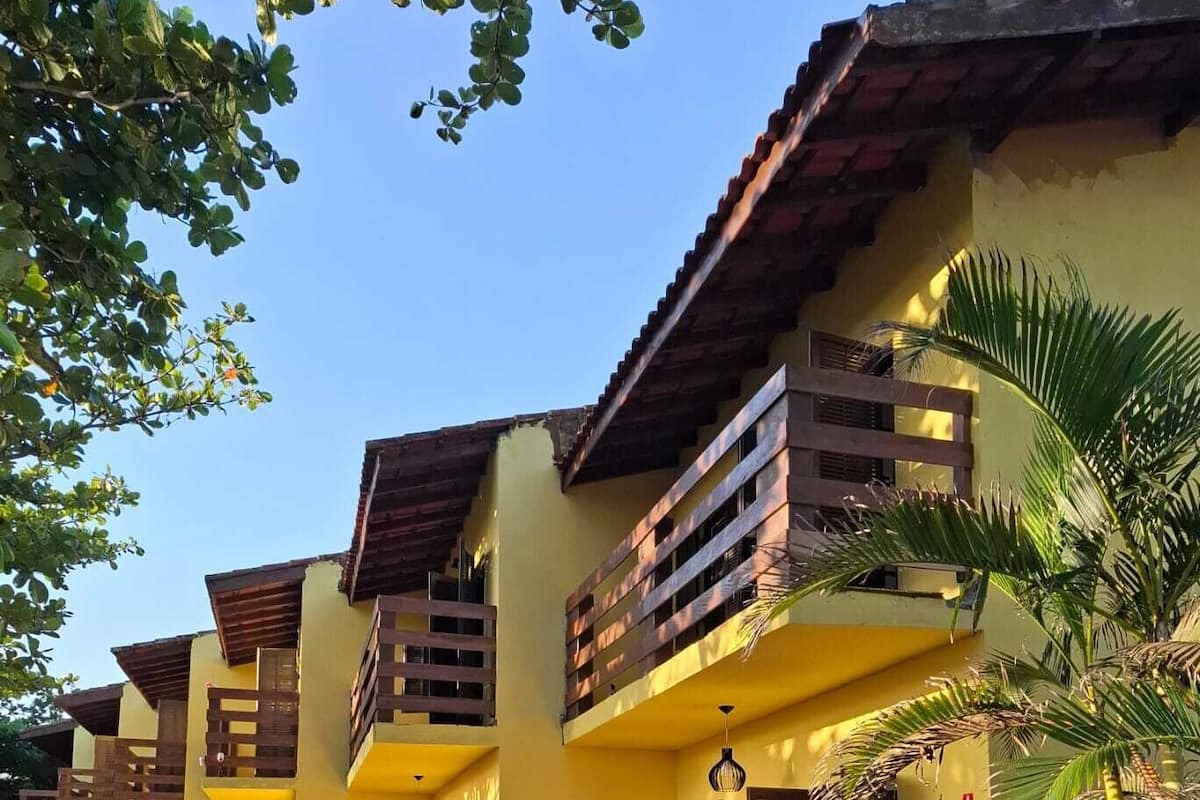 Un bâtiment jaune doté d’un balcon, d’un palmier et d’un petit jardin.