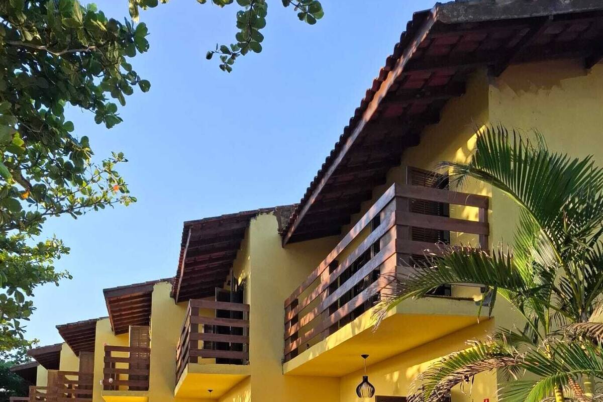 A yellow building with a balcony, a palm tree, and a small garden area.