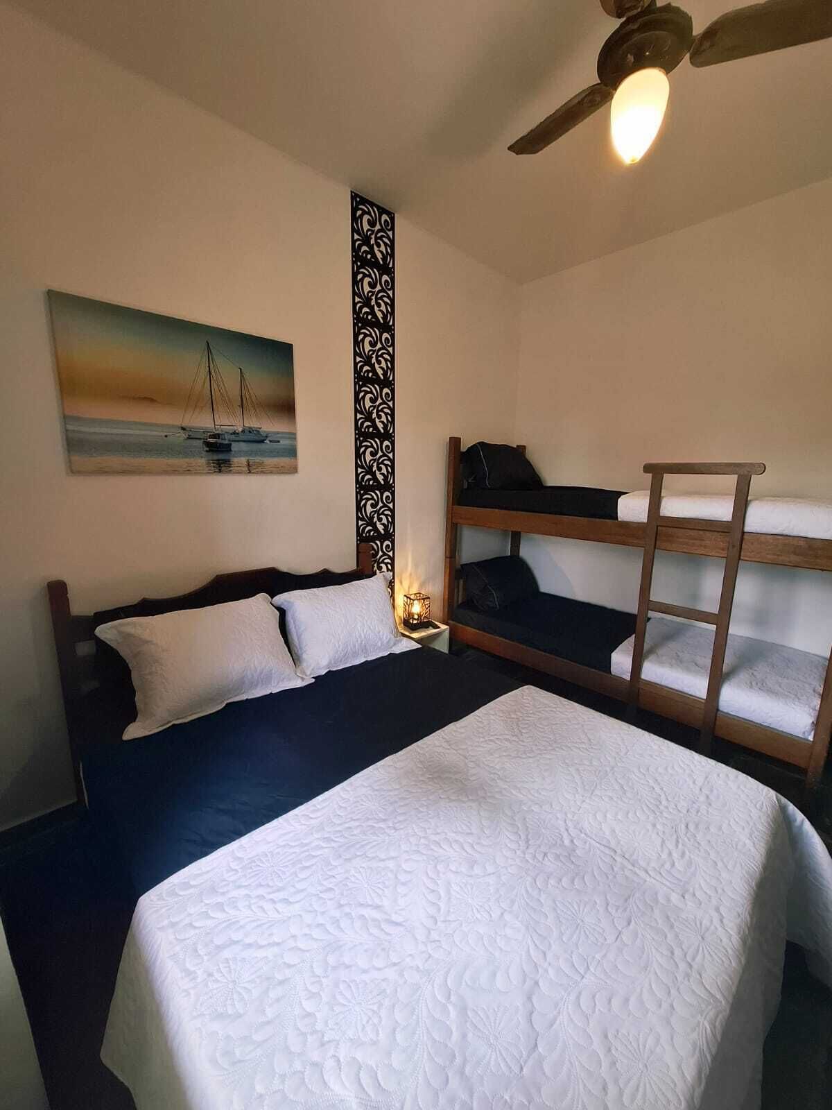 A bedroom with a single bed, a bunk bed, a ceiling fan, and a painting of a sailboat on the wall.