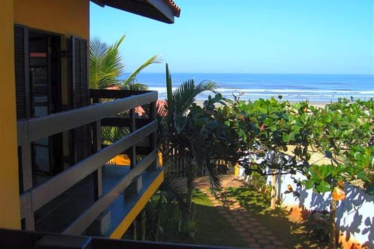 Un balcon avec vue sur l’océan, un chemin bordé d’arbres et des plantes tropicales.