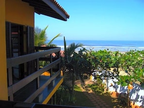 A balcony with a view of the ocean, a checkered pathway, and tropical plants.