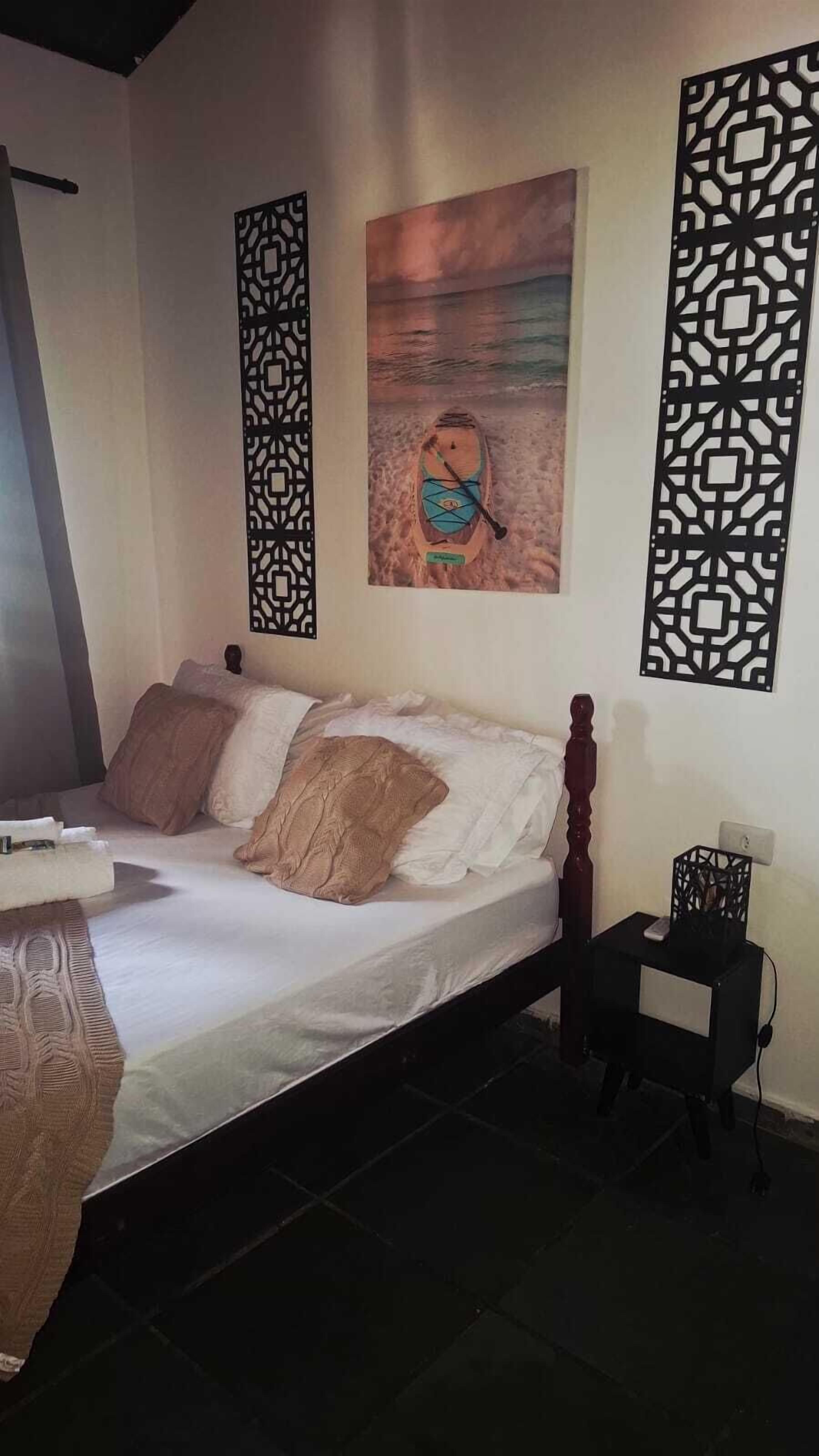 A bedroom with a bed, a nightstand, a decorative wall panel, and a painting of a boat on the wall.
