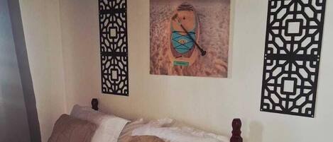 A bedroom with a bed, a nightstand, a decorative wall panel, and a painting of a boat on the wall.