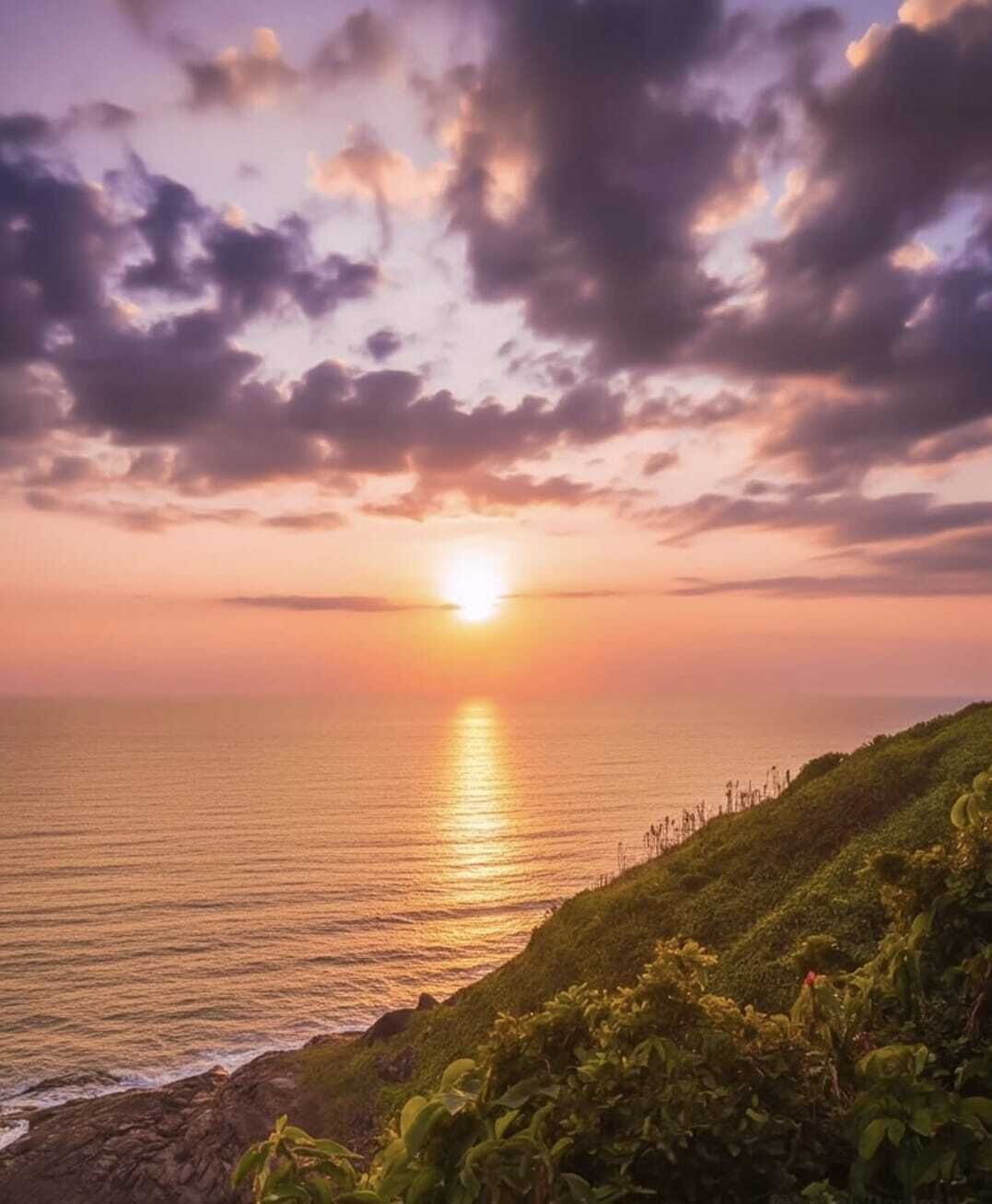Um pôr do sol sobre uma paisagem costeira com falésias e vegetação densa.