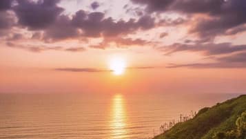 Um pôr do sol sobre uma paisagem costeira com falésias e vegetação densa.