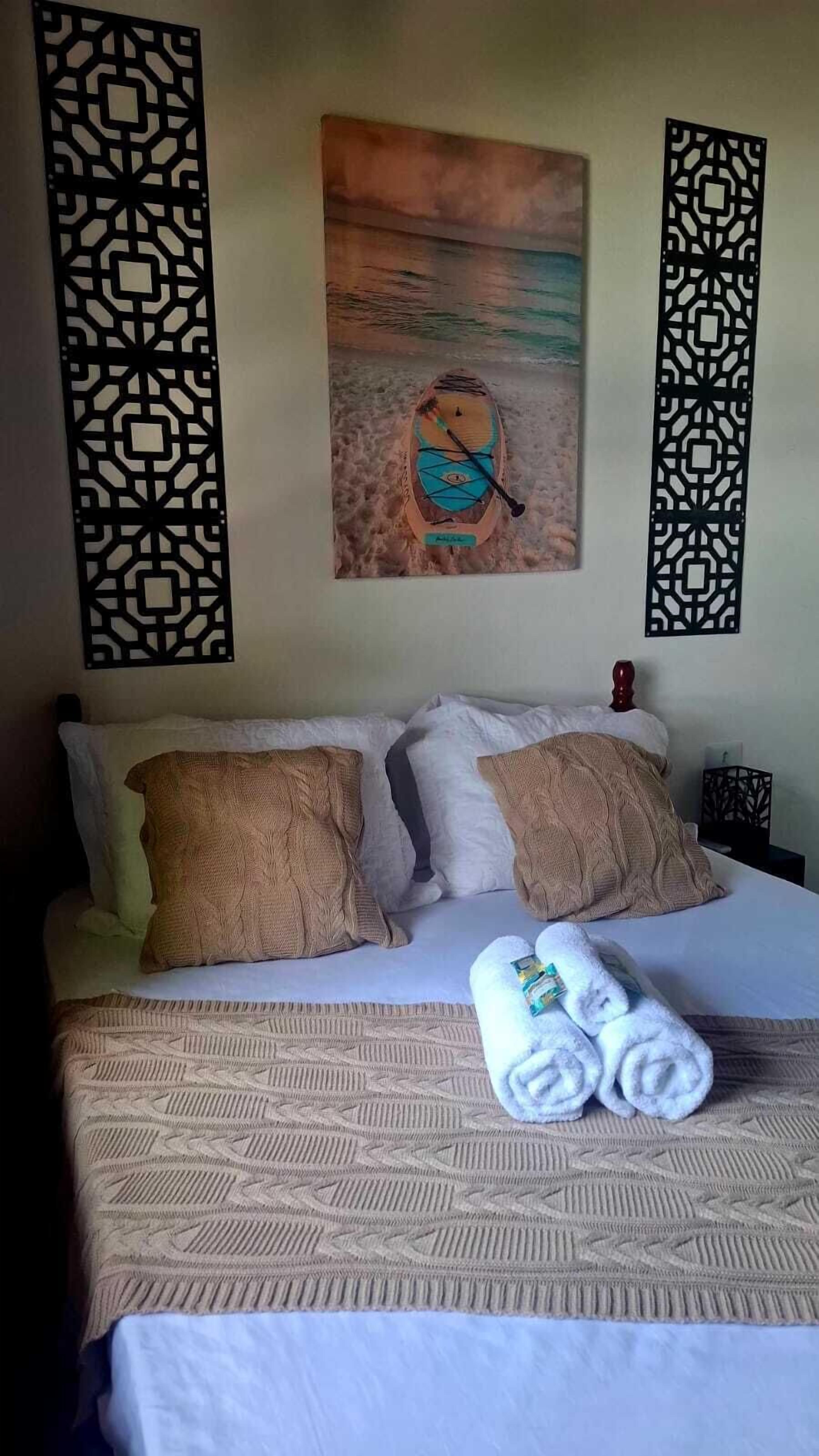 A hotel room with a bed, pillows, a painting, and a decorative screen.