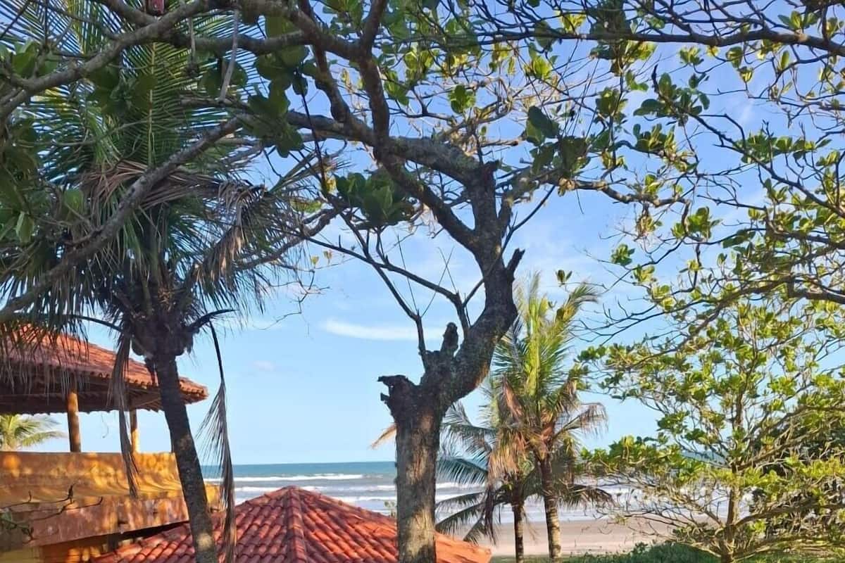 Une vue côtière avec une maison dont le toit est recouvert de tuiles rouges, des palmiers et une plage en arrière-plan.