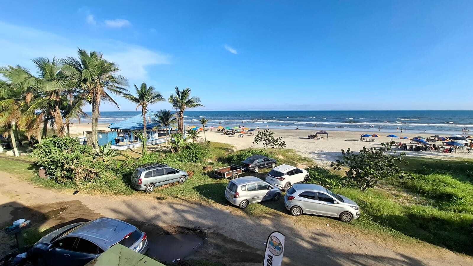 Un parking situé au bord de la plage, avec plusieurs voitures, des palmiers et une vue sur l’océan.
