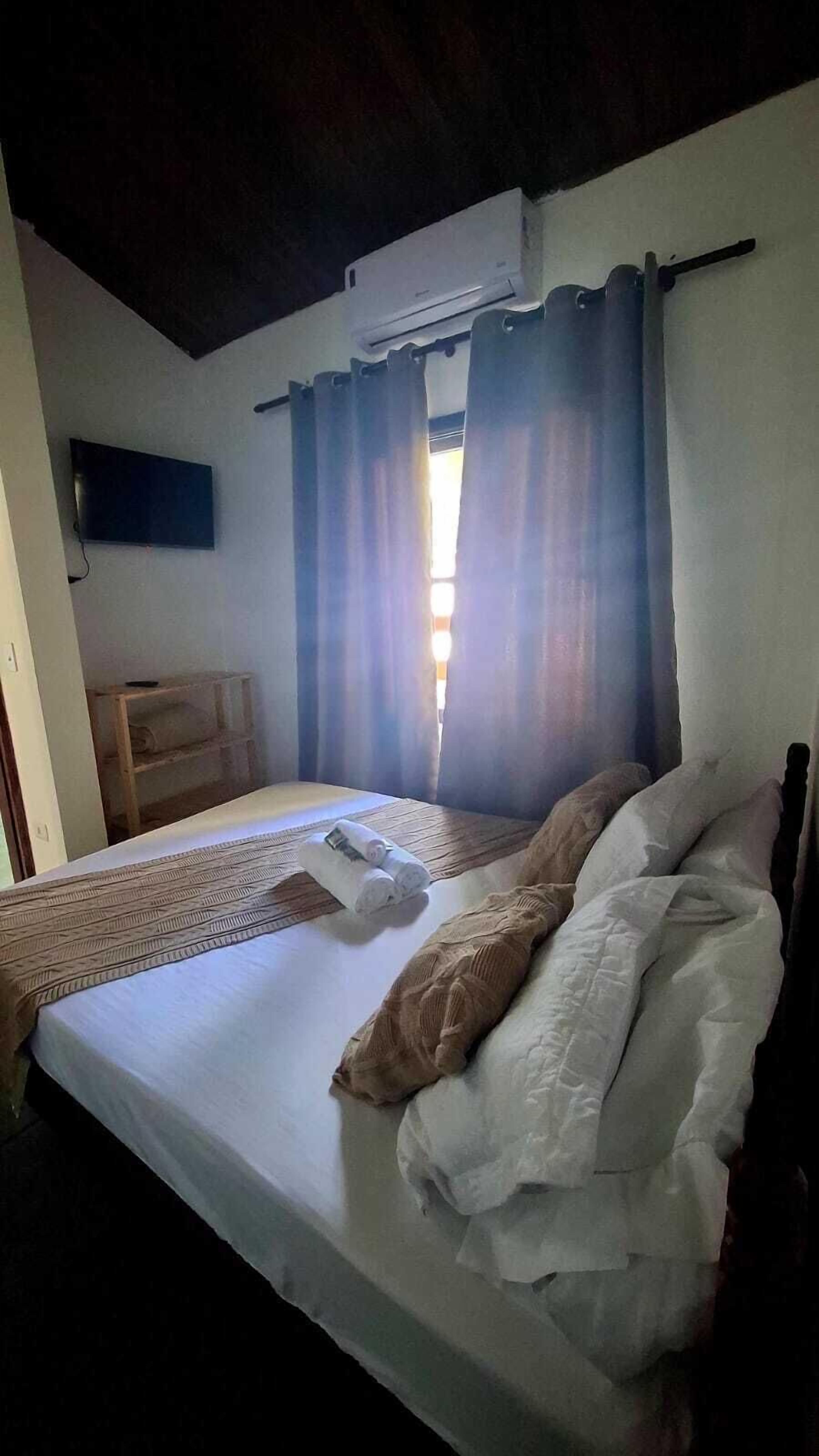 Quarto com uma cama, televisão na parede e janela com cortinas.